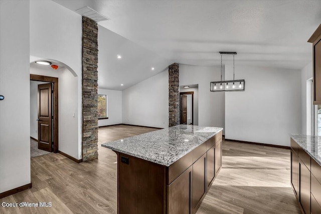 kitchen featuring light hardwood / wood-style floors, light stone counters, vaulted ceiling, and a center island