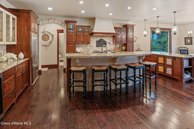 kitchen with a breakfast bar, dark hardwood / wood-style floors, premium range hood, a spacious island, and pendant lighting