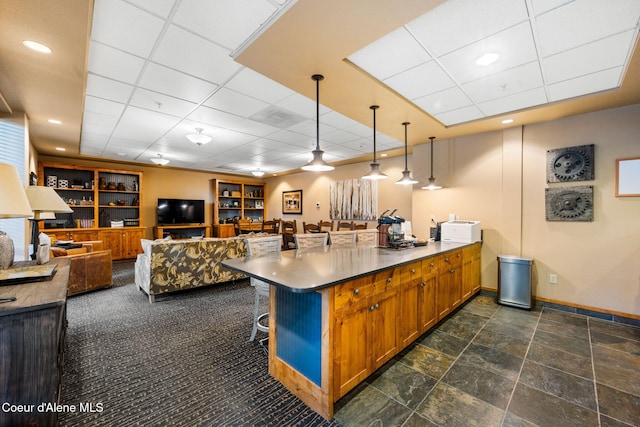 kitchen with built in shelves, a paneled ceiling, hanging light fixtures, a breakfast bar, and kitchen peninsula