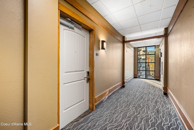 corridor with a paneled ceiling and dark carpet