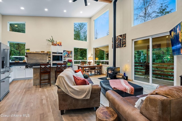 living room with plenty of natural light, light hardwood / wood-style floors, a wood stove, and a towering ceiling