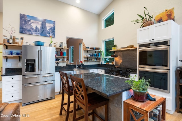 kitchen featuring sink, high vaulted ceiling, appliances with stainless steel finishes, white cabinets, and light wood-type flooring