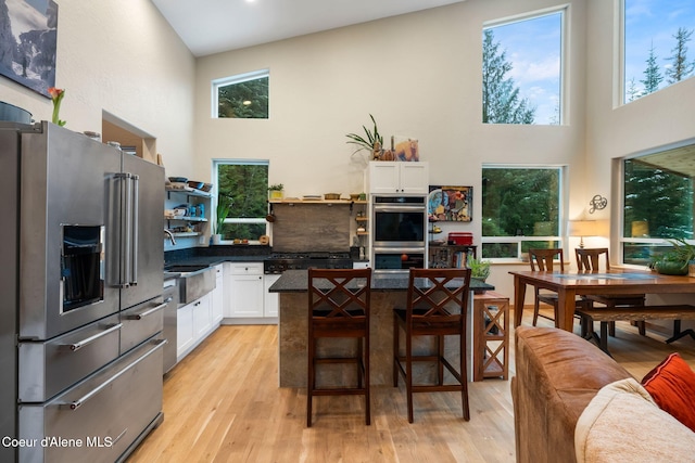 kitchen featuring appliances with stainless steel finishes, a kitchen breakfast bar, high vaulted ceiling, white cabinets, and light hardwood / wood-style floors