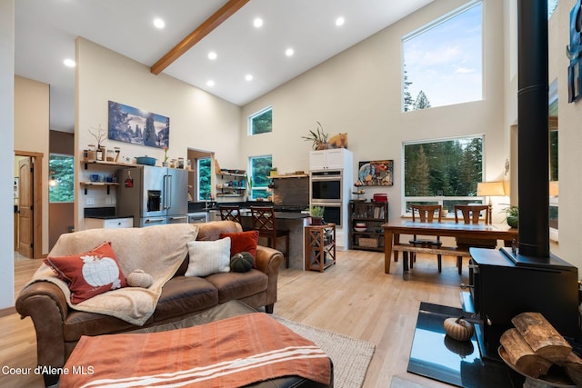 living room with beamed ceiling, light wood-type flooring, high vaulted ceiling, and a wood stove