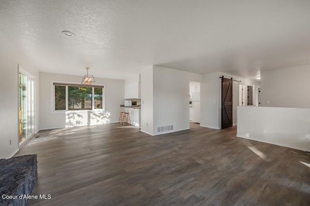 14895 N Crystal Springs Ln, Rathdrum, ID 83858 - unfurnished living room with a barn door, dark wood-style floors, a textured ceiling, and baseboards