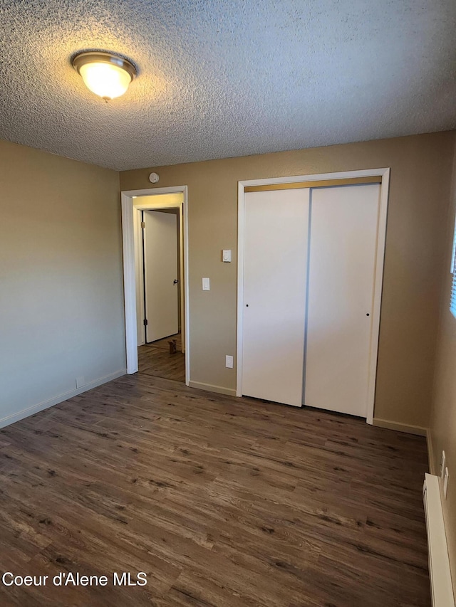 unfurnished bedroom featuring dark wood-type flooring, a baseboard radiator, a closet, and a textured ceiling