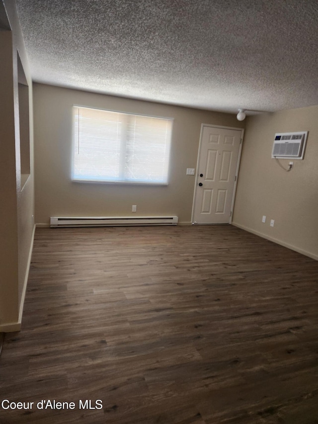 interior space with dark hardwood / wood-style floors, a textured ceiling, baseboard heating, and a wall mounted air conditioner