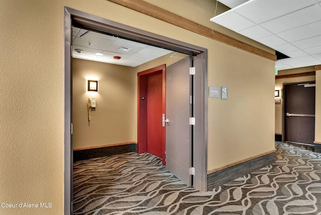 hallway with a paneled ceiling and dark colored carpet