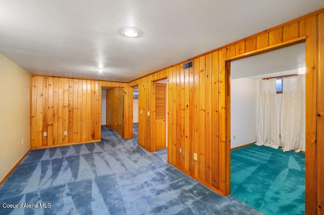 carpeted empty room featuring wooden walls