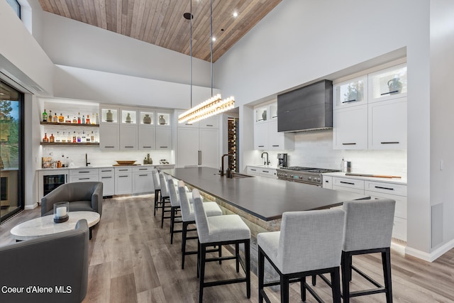 kitchen with a center island with sink, white cabinets, high vaulted ceiling, decorative light fixtures, and premium range hood