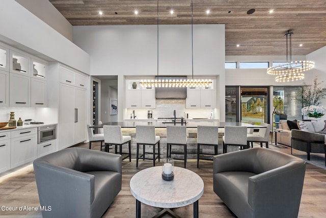 living room featuring a towering ceiling, a notable chandelier, sink, light hardwood / wood-style floors, and wooden ceiling