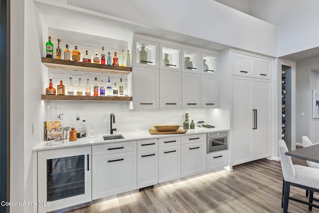 bar featuring wine cooler, light hardwood / wood-style flooring, sink, and white cabinets