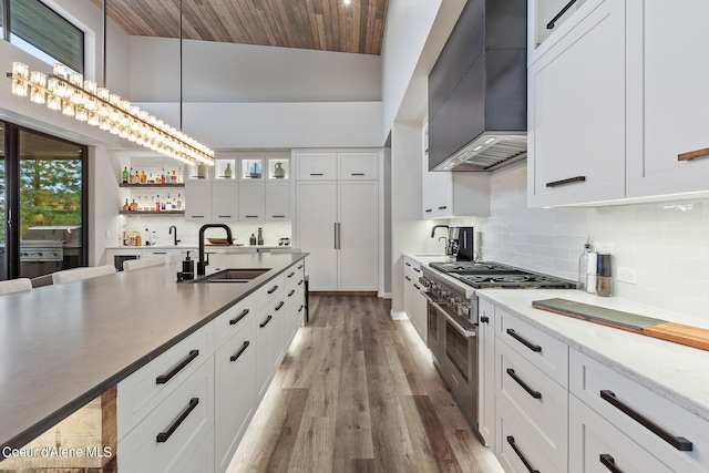 kitchen featuring double oven range, sink, hardwood / wood-style flooring, white cabinets, and wall chimney exhaust hood