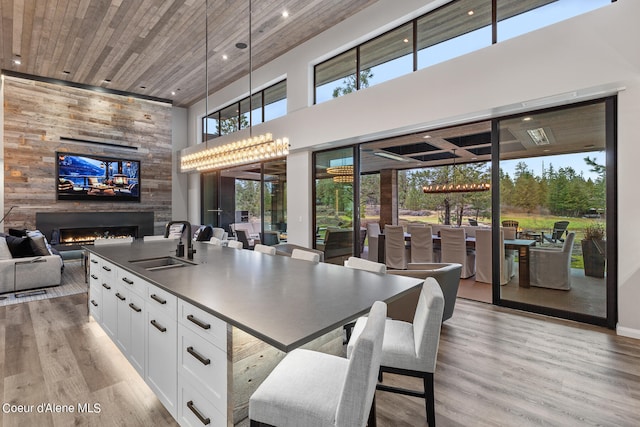 kitchen featuring a towering ceiling, hanging light fixtures, sink, light hardwood / wood-style floors, and white cabinets