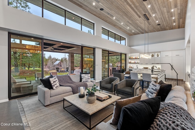 living room featuring a high ceiling, light wood-type flooring, sink, and wooden ceiling