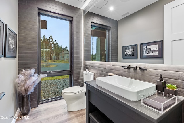 bathroom with toilet, vanity, wood-type flooring, and tile walls