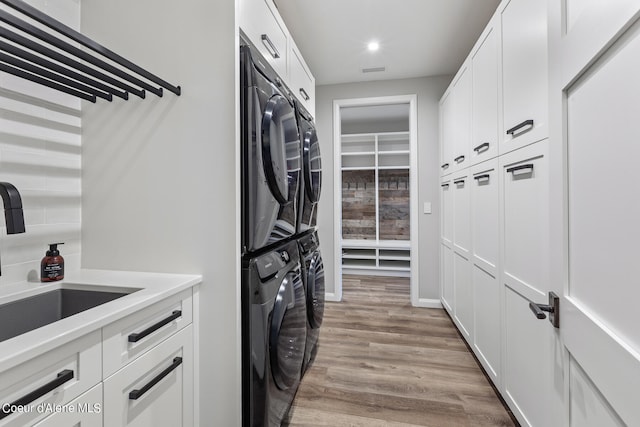 clothes washing area featuring light wood-type flooring, cabinets, sink, and stacked washer and dryer