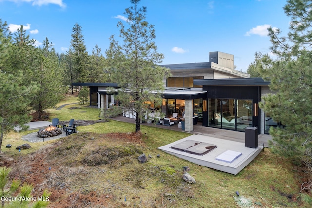 rear view of property with a lawn, a patio, and an outdoor living space with a fire pit