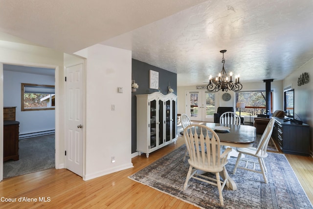 dining room with a chandelier, a textured ceiling, light wood-type flooring, and a baseboard heating unit