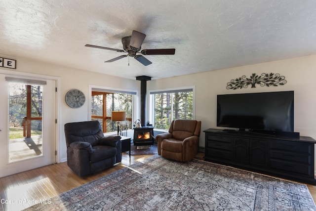 living room featuring a textured ceiling, light hardwood / wood-style flooring, a wood stove, and ceiling fan