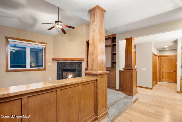 unfurnished living room featuring ornate columns, light hardwood / wood-style floors, a textured ceiling, ceiling fan, and a tile fireplace