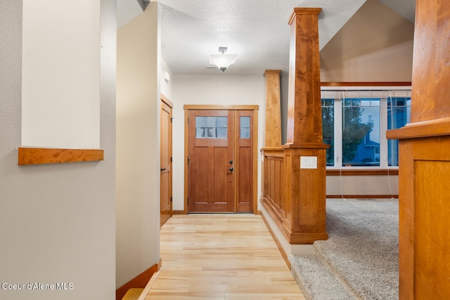 doorway to outside with a textured ceiling, light hardwood / wood-style flooring, and vaulted ceiling