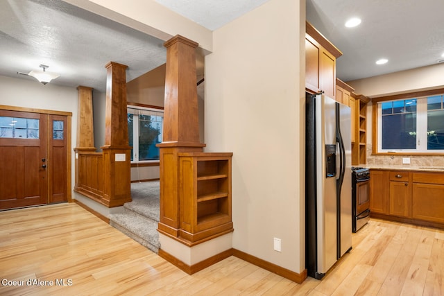 kitchen with stainless steel fridge, light wood-type flooring, black gas range oven, and ornate columns