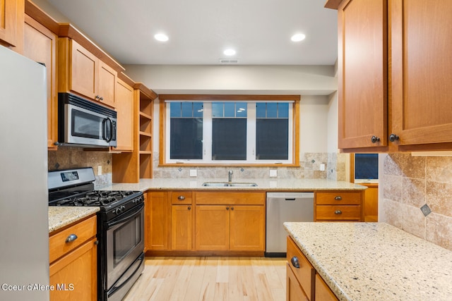 kitchen with sink, appliances with stainless steel finishes, light wood-type flooring, and light stone counters