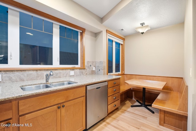 kitchen with decorative backsplash, light stone countertops, sink, light hardwood / wood-style flooring, and dishwasher