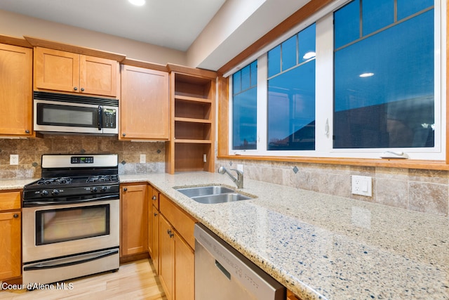 kitchen with light stone countertops, sink, stainless steel appliances, tasteful backsplash, and light hardwood / wood-style floors