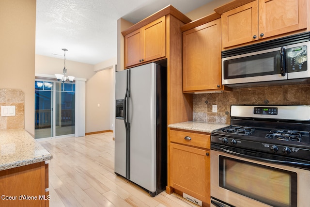 kitchen with light hardwood / wood-style floors, a chandelier, backsplash, light stone countertops, and stainless steel appliances