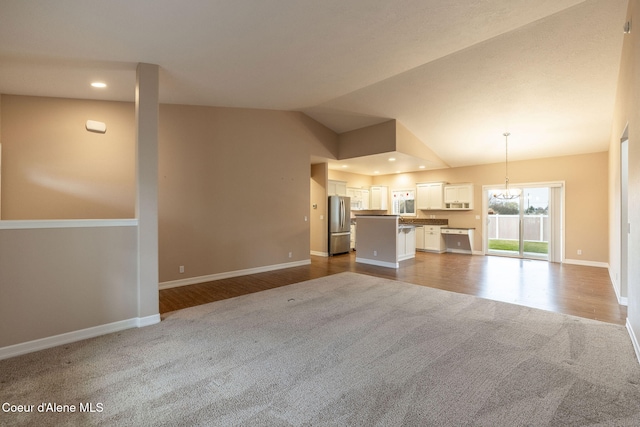 unfurnished living room featuring hardwood / wood-style floors, a notable chandelier, and vaulted ceiling