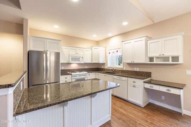 kitchen with white appliances, light hardwood / wood-style flooring, dark stone countertops, a kitchen island, and white cabinetry