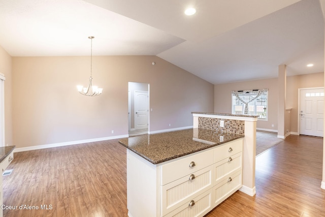 kitchen with hanging light fixtures, dark stone counters, vaulted ceiling, and light wood-type flooring