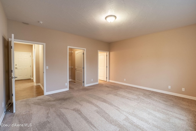 unfurnished bedroom featuring light colored carpet, a walk in closet, and a textured ceiling