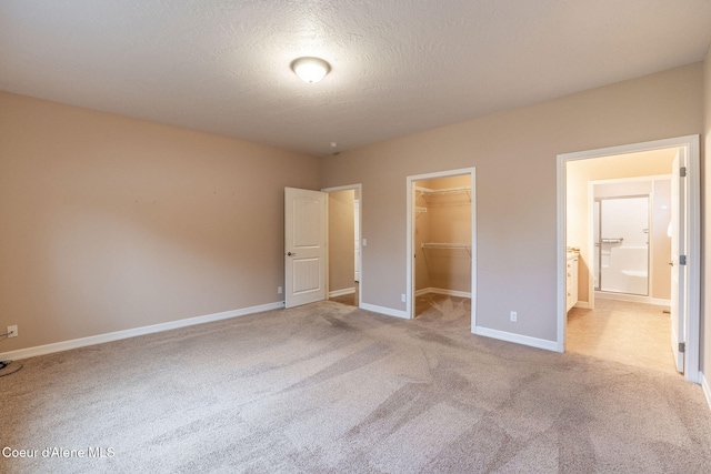 unfurnished bedroom featuring ensuite bathroom, light colored carpet, a textured ceiling, a walk in closet, and a closet