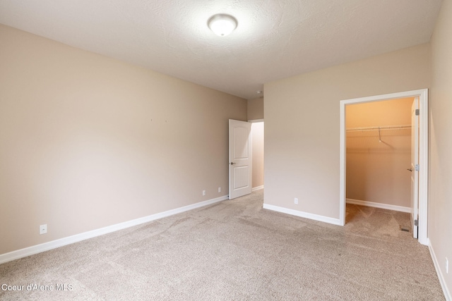 unfurnished bedroom with a textured ceiling, a spacious closet, light carpet, and a closet