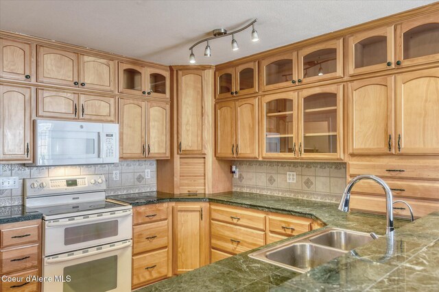 kitchen featuring a sink, decorative backsplash, white appliances, and glass insert cabinets