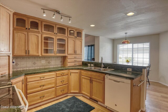 kitchen featuring backsplash, dishwasher, a sink, a peninsula, and light wood-style flooring