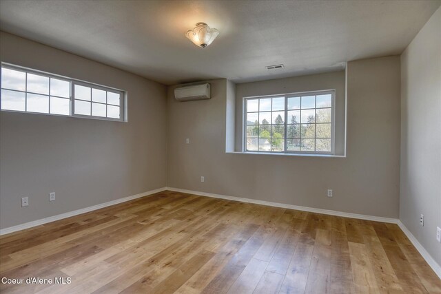 empty room featuring an AC wall unit, baseboards, visible vents, and wood finished floors