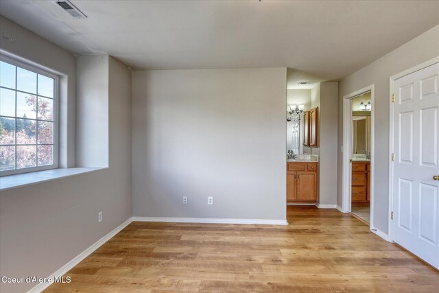 unfurnished bedroom featuring visible vents, baseboards, light wood finished floors, and ensuite bath
