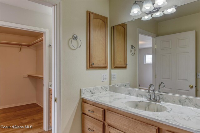 bathroom featuring vanity, baseboards, a walk in closet, and wood finished floors