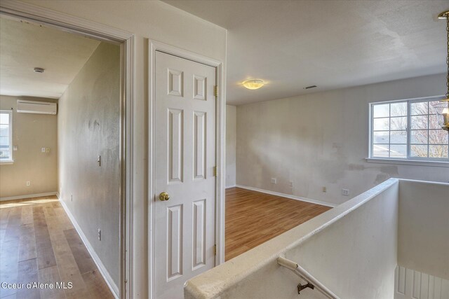 corridor with a wall unit AC, wood finished floors, and a wealth of natural light