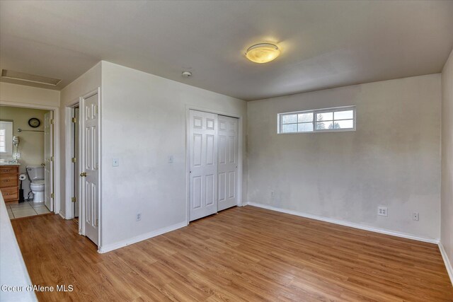 unfurnished bedroom featuring baseboards, attic access, light wood finished floors, and a closet