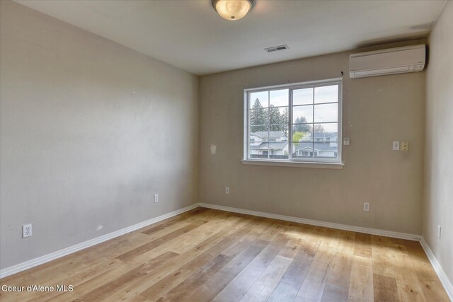 spare room with visible vents, a wall mounted air conditioner, light wood-style flooring, and baseboards