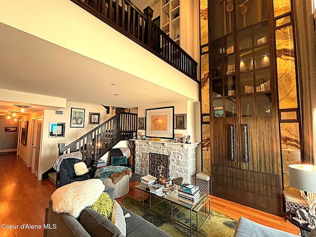 living room with a high ceiling, wood-type flooring, and a stone fireplace