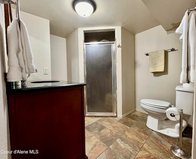 bathroom featuring a textured ceiling, vanity, toilet, and a shower with shower door