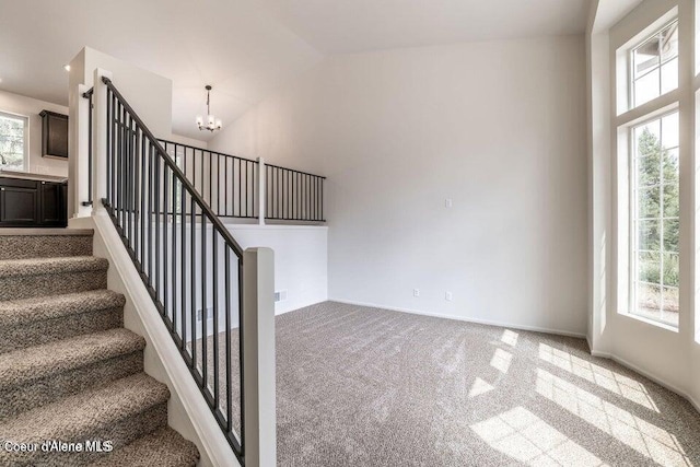 staircase featuring carpet, a notable chandelier, lofted ceiling, and a wealth of natural light