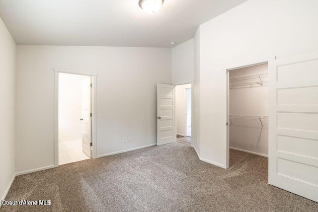 unfurnished bedroom with a walk in closet, a closet, light colored carpet, and lofted ceiling