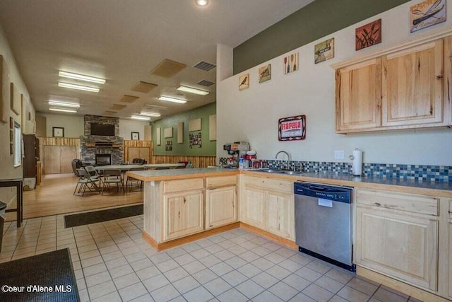 kitchen with dishwasher, sink, a stone fireplace, kitchen peninsula, and light brown cabinetry